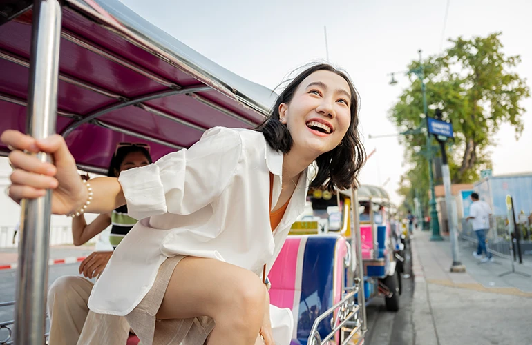 Mujer sonriendo mientras viaja en un tuk tuk por las calles de Tailandia