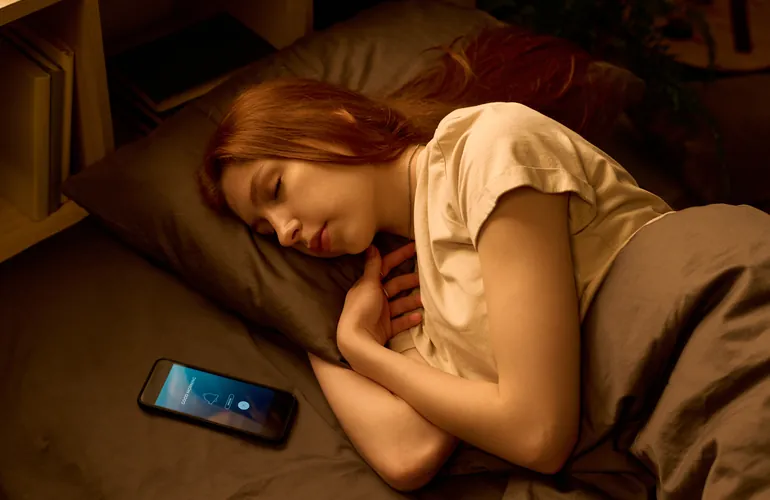 Mujer durmiendo con el móvil apartado tras apagar las pantallas antes de dormir